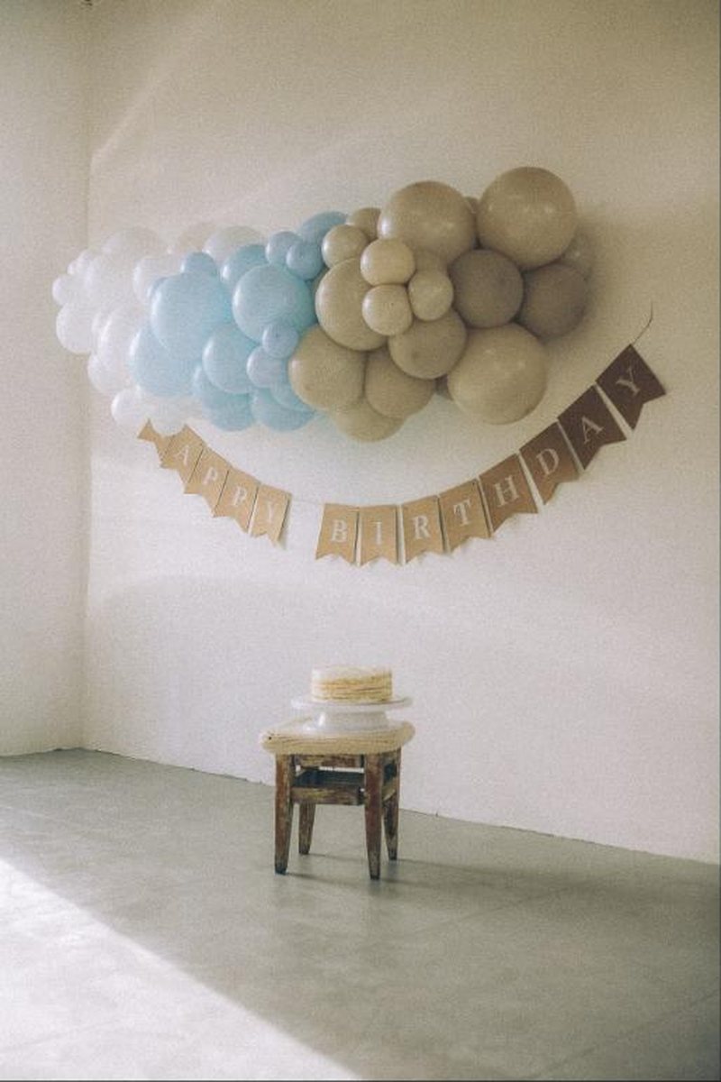 Soft neutral balloon garland with a birthday banner and cake